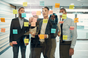 Business team collaborating around a glass wall covered with sticky notes during a strategic planning session.